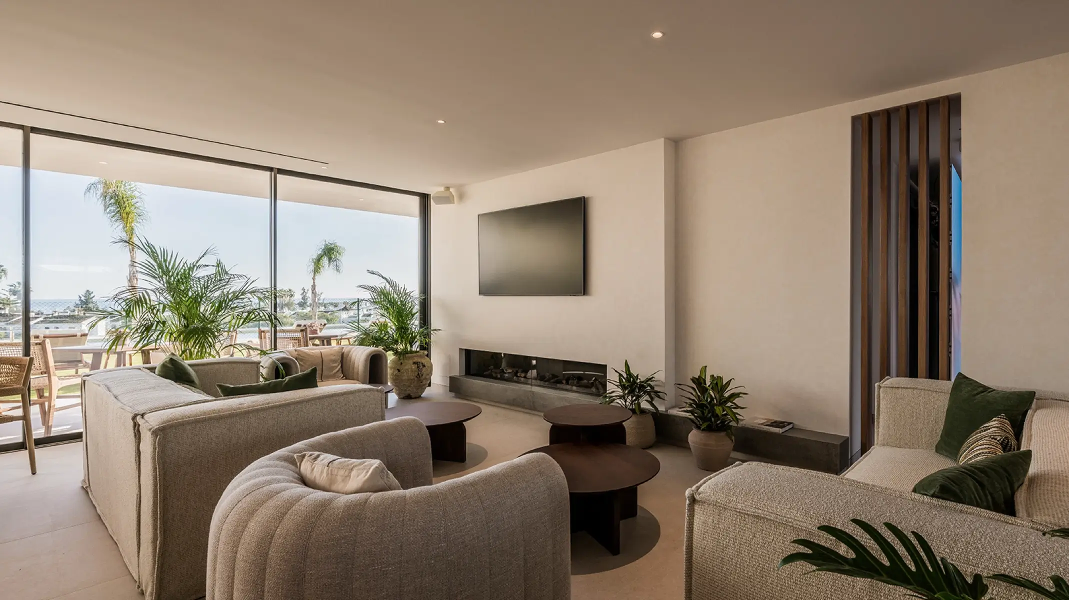 Salón común de Naghoi — ventanales de suelo a techo con vistas al mar, chimenea y asientos confortables, centro de recuperación postoperatoria en Marbella.