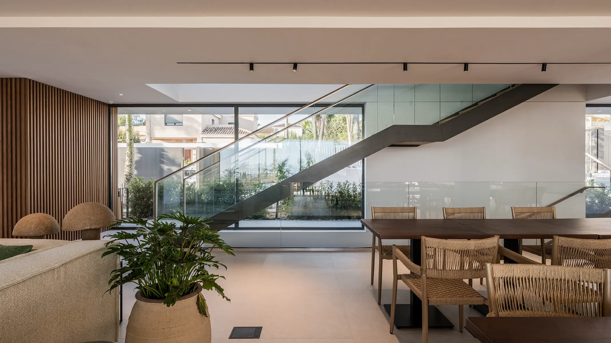 Zona de comedor común de Naghoi — interior diáfano con escalera de cristal y vistas al jardín dentro del santuario de recuperación de Facialteam.