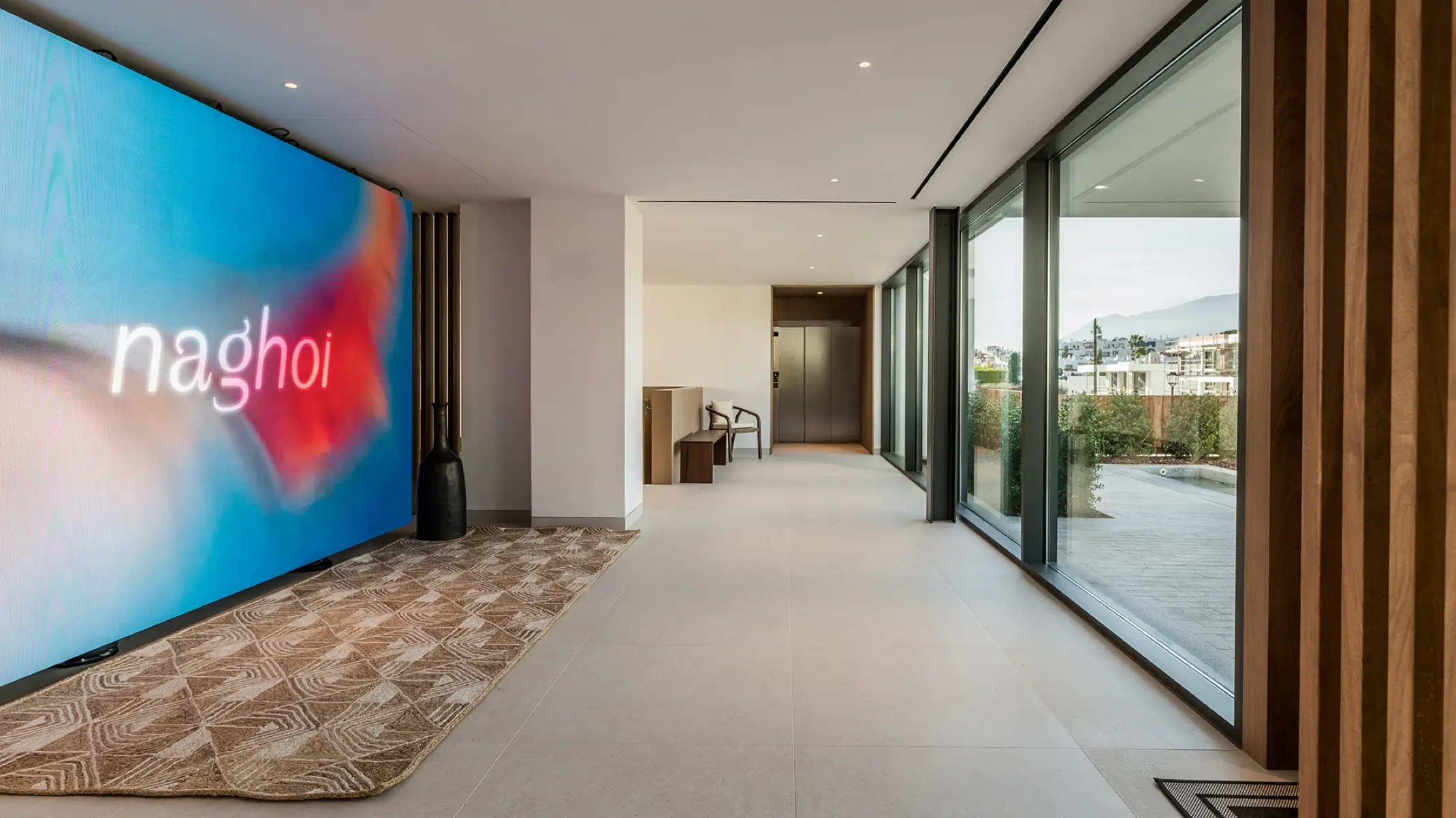 Vestíbulo de entrada de Naghoi — interior moderno con ventanales de suelo a techo con vistas a los jardines del santuario de recuperación de Facialteam en Marbella.